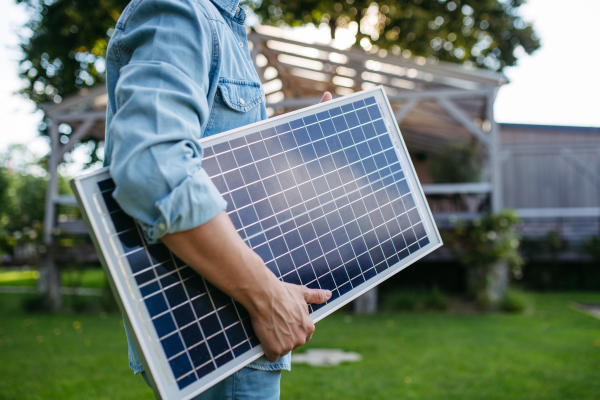 Man looking at solar panel in arms, standing in garden. Sustainable lifestyle and green household, home.