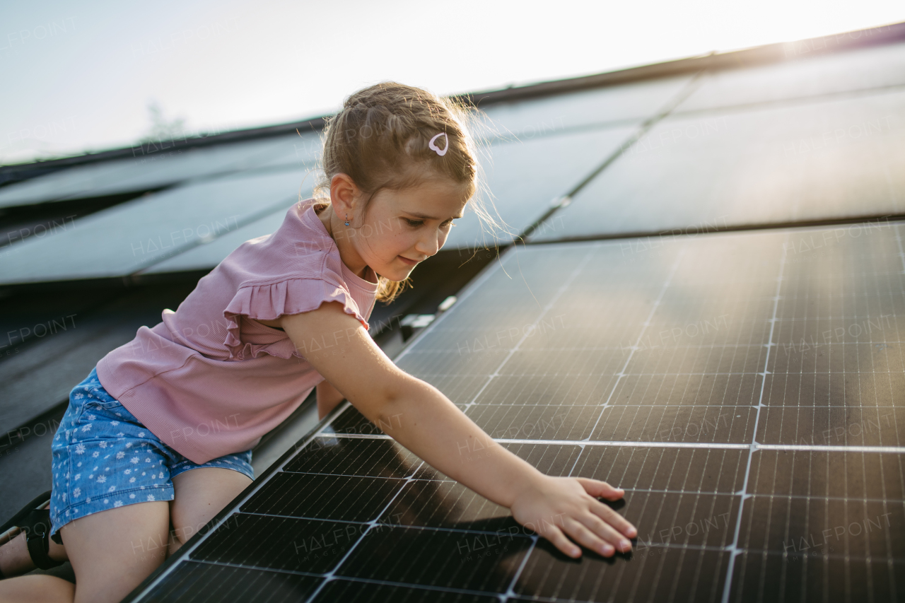 Cute girl sitting on solar panels roof, touching panel with hand.Rooftop solar or photovoltaic system. Sustainable future for next generation concept.