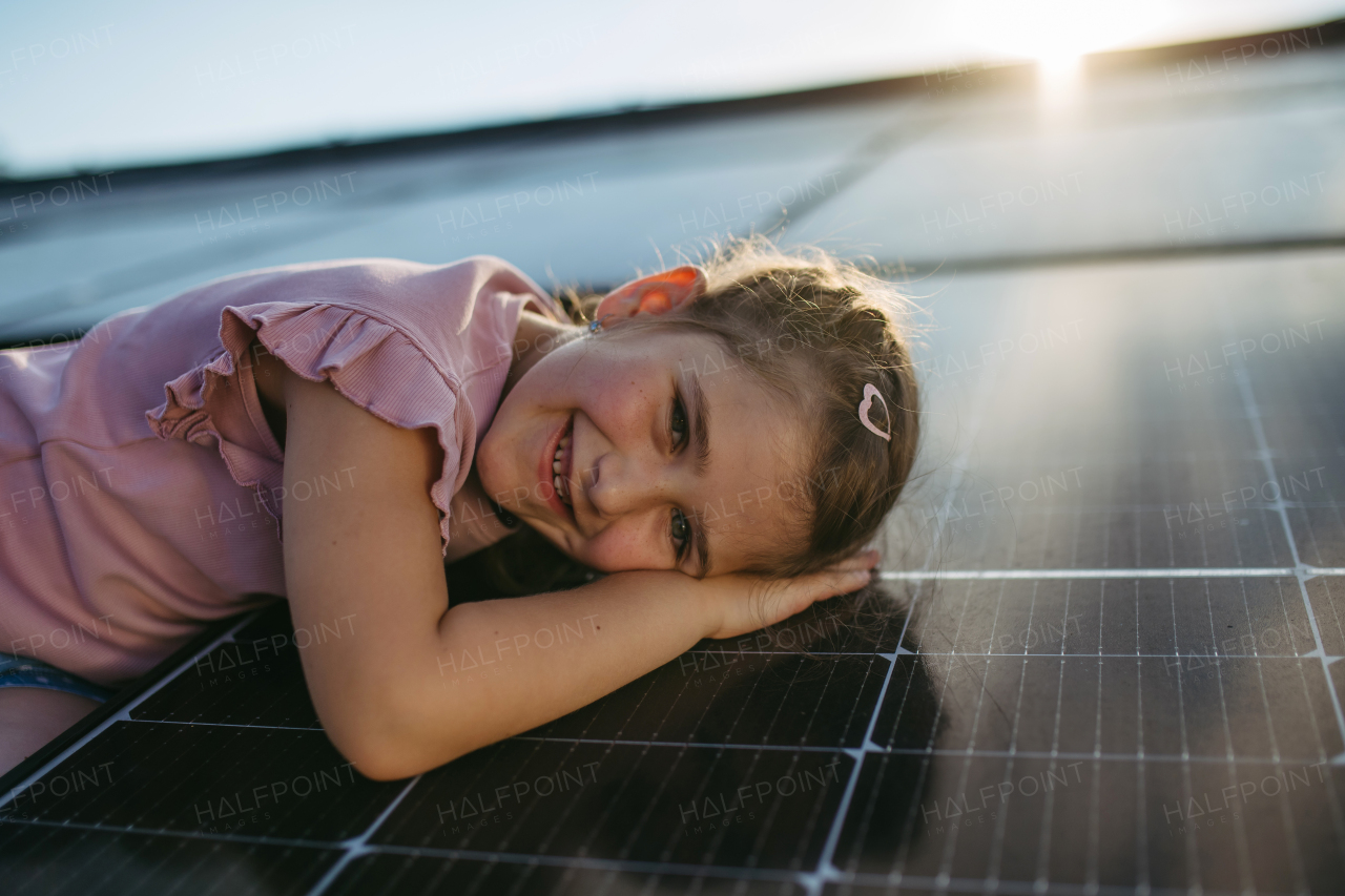 Cute girl lying on solar panels roof, shot with copy space. Rooftop solar or photovoltaic system. Sustainable future for next generation concept.