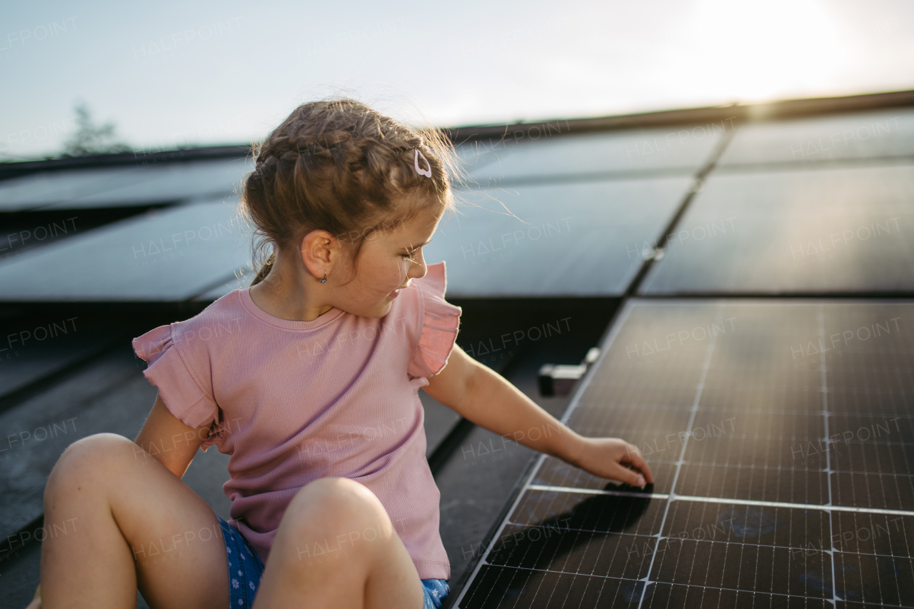 Cute girl on roof with solar panels, standing with open arms, hands up in the air. Rooftop solar or photovoltaic system. Sustainable future for next generation concept.