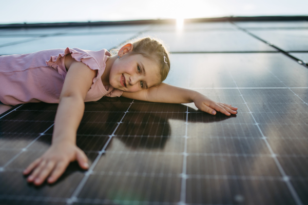 Cute girl lying on solar panels roof, shot with copy space. Rooftop solar or photovoltaic system. Sustainable future for next generation concept.