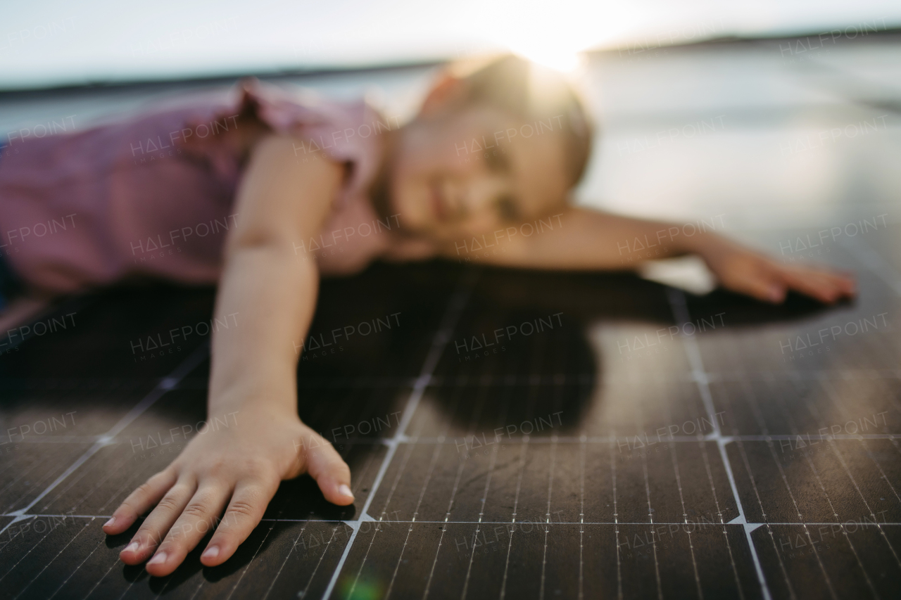 Cute girl lying on solar panels roof, close up on hand.Rooftop solar or photovoltaic system. Sustainable future for next generation concept.