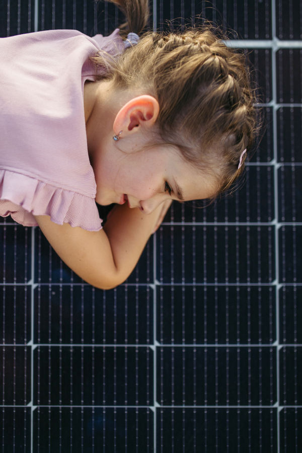 Cute girl lying on solar panels on the roof, shot with copy space. Rooftop solar or photovoltaic system. Sustainable future for next generation concept.