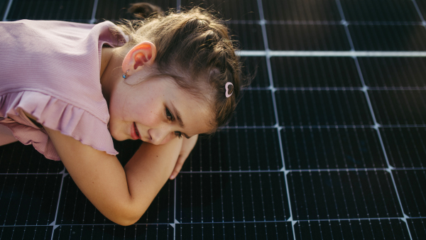 Cute girl lying on solar panels roof, shot with copy space. Rooftop solar or photovoltaic system. Sustainable future for next generation concept.