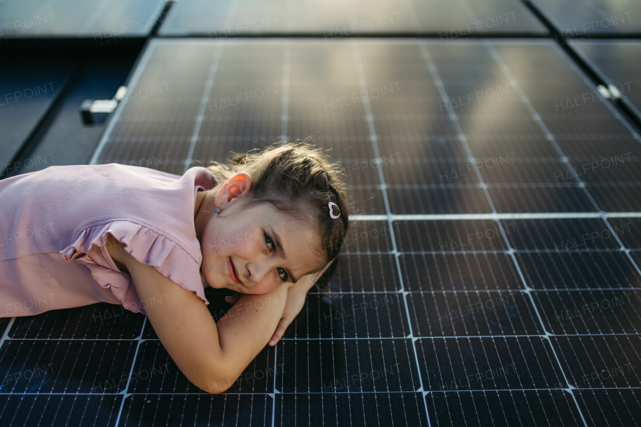 Cute girl lying on solar panels on the roof, shot with copy space. Rooftop solar or photovoltaic system. Sustainable future for next generation concept.