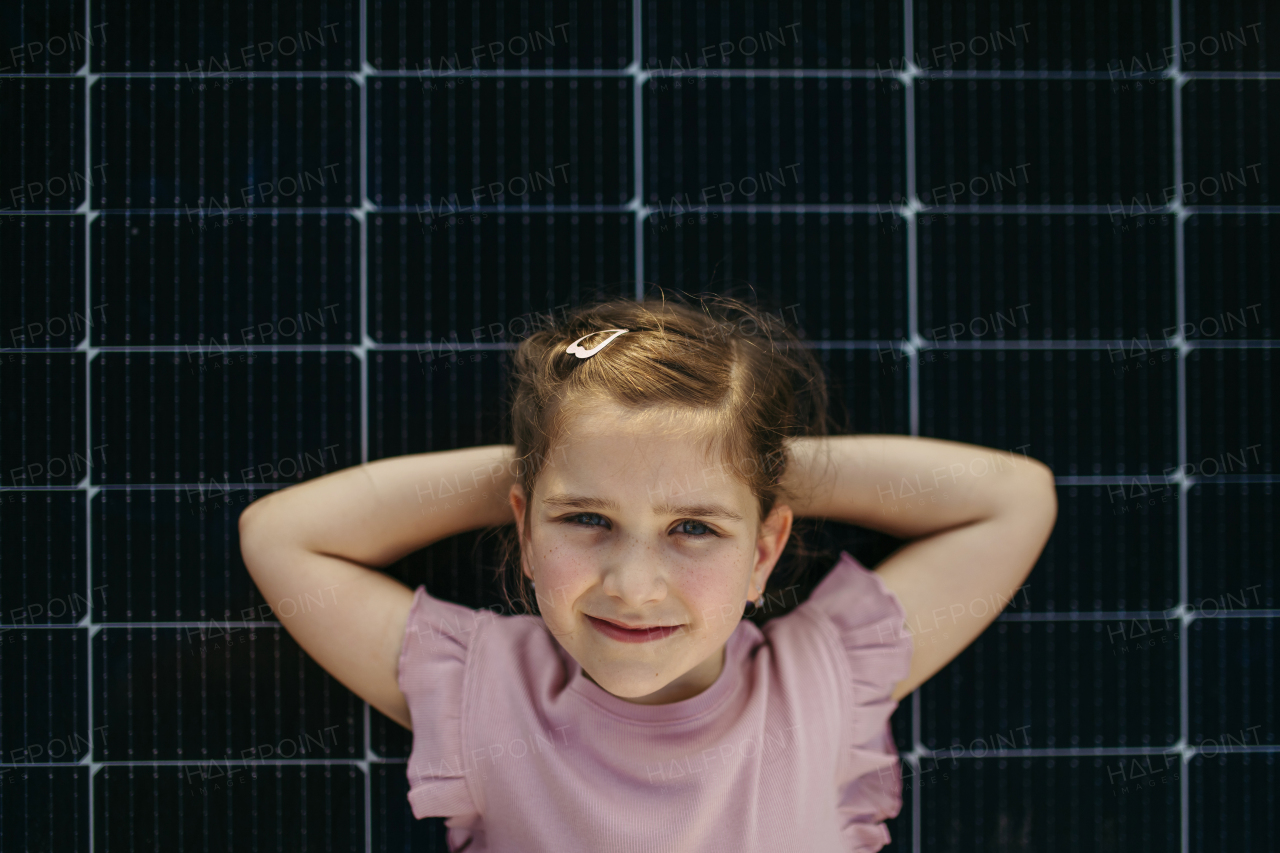 Top view of girl lying on solar panels roof, looking at camera. Rooftop solar or photovoltaic system. Sustainable future for next generation concept.