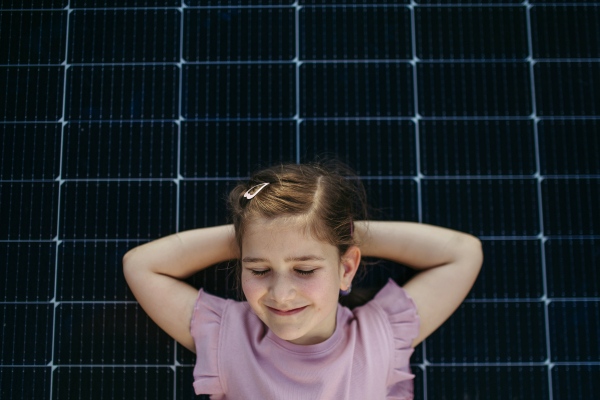 Cute girl lying on solar panels roof, shot with copy space. Rooftop solar or photovoltaic system. Sustainable future for next generation concept.