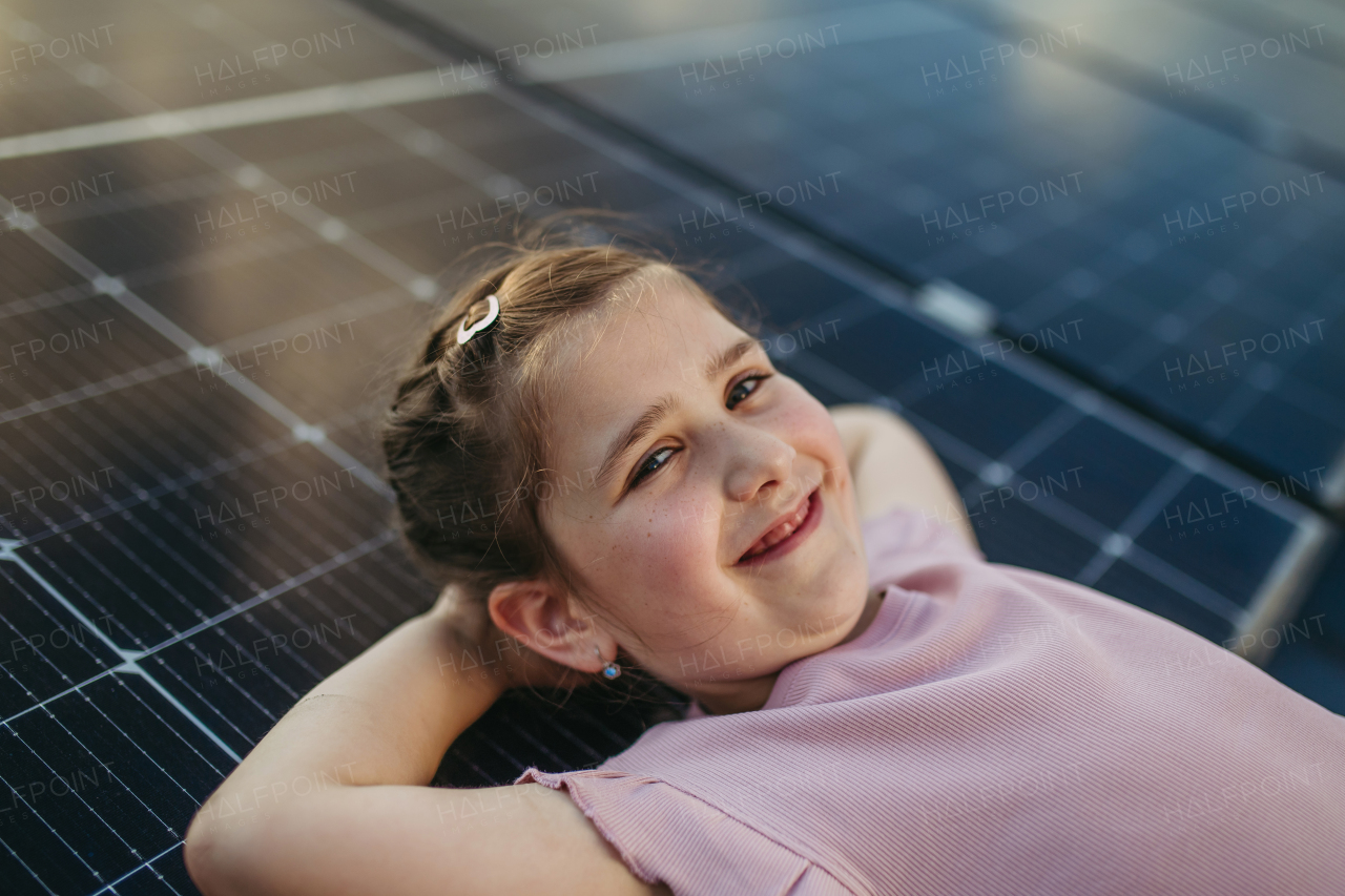 Cute girl lying on solar panels roof, shot with copy space. Rooftop solar or photovoltaic system. Sustainable future for next generation concept.