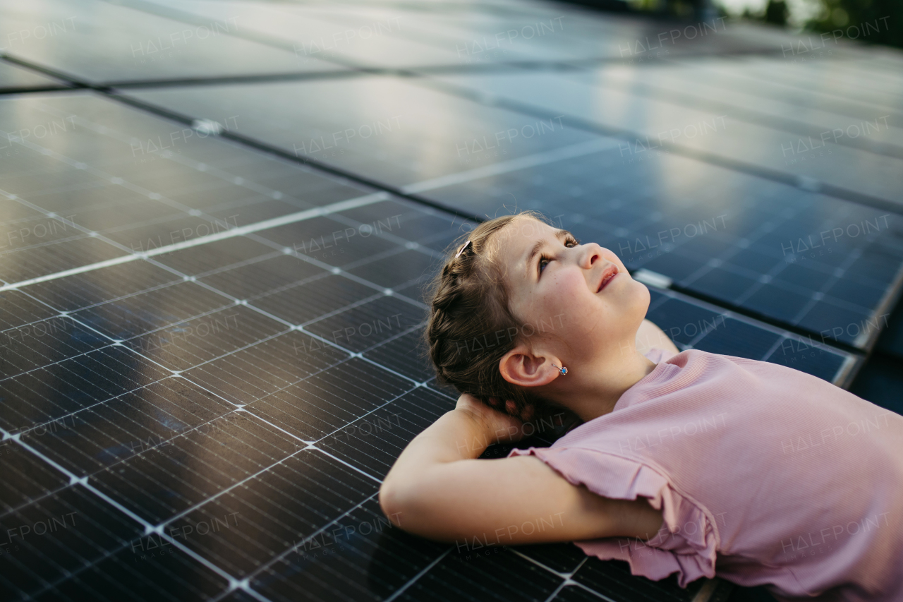 Cute girl lying on solar panels roof, shot with copy space. Rooftop solar or photovoltaic system. Sustainable future for next generation concept.