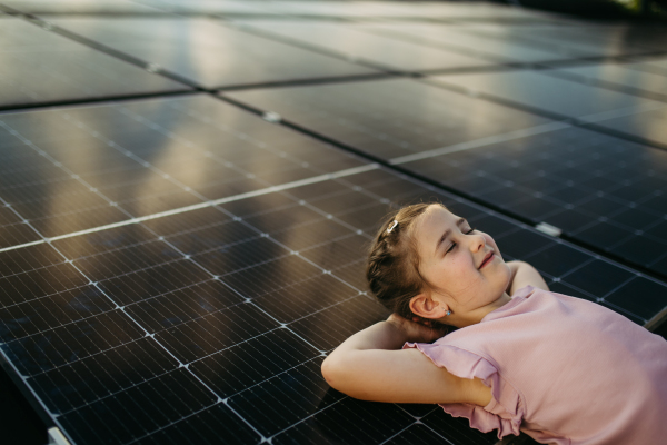 Cute girl lying on solar panels roof, shot with copy space. Rooftop solar or photovoltaic system. Sustainable future for next generation concept.