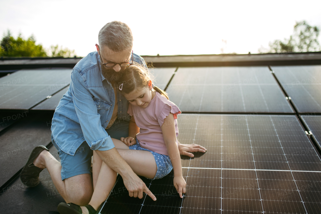 Dad and girl on roof with solar panels, learning about solar energy. Rooftop solar or photovoltaic system. Sustainable future for next generation concept.