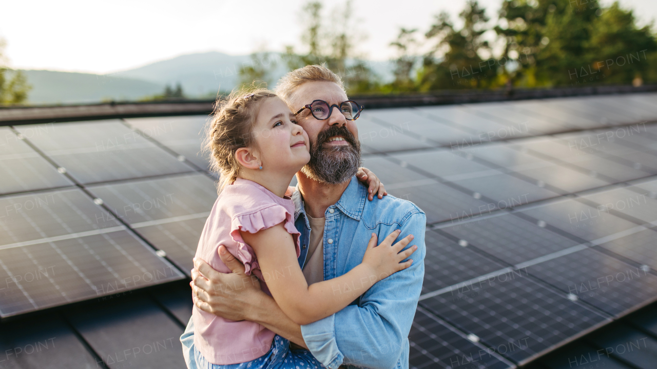 Father with girl on roof with solar panels, hugging, looking at sky. Rooftop solar or photovoltaic system. Sustainable future for next generation concept.