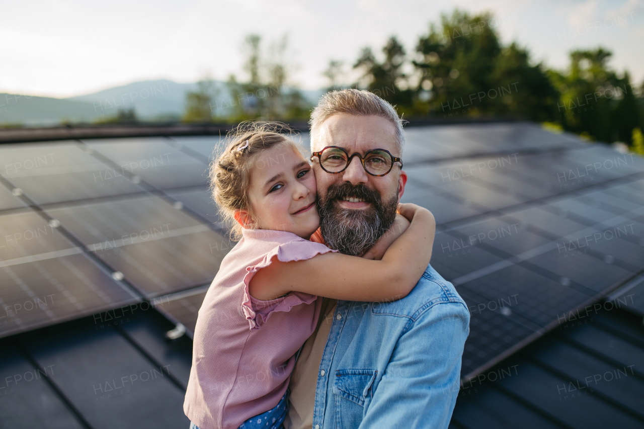 Father with girl on roof with solar panels, hugging. Rooftop solar or photovoltaic system. Sustainable future for next generation concept.