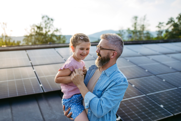 Father with girl on roof with solar panels, hugging. Rooftop solar or photovoltaic system. Sustainable future for next generation concept.