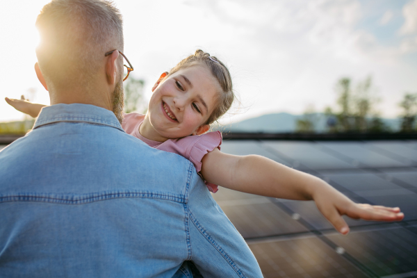 Father with girl on roof with solar panels, hugging. Rooftop solar or photovoltaic system. Sustainable future for next generation concept.