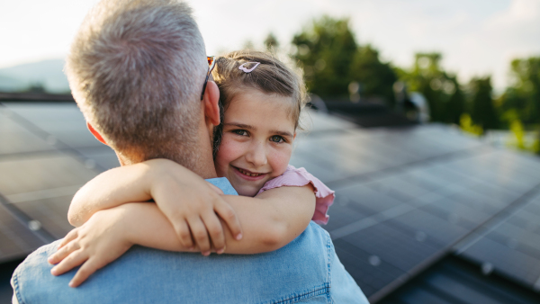 Father with girl on roof with solar panels, hugging. Rooftop solar or photovoltaic system. Sustainable future for next generation concept.