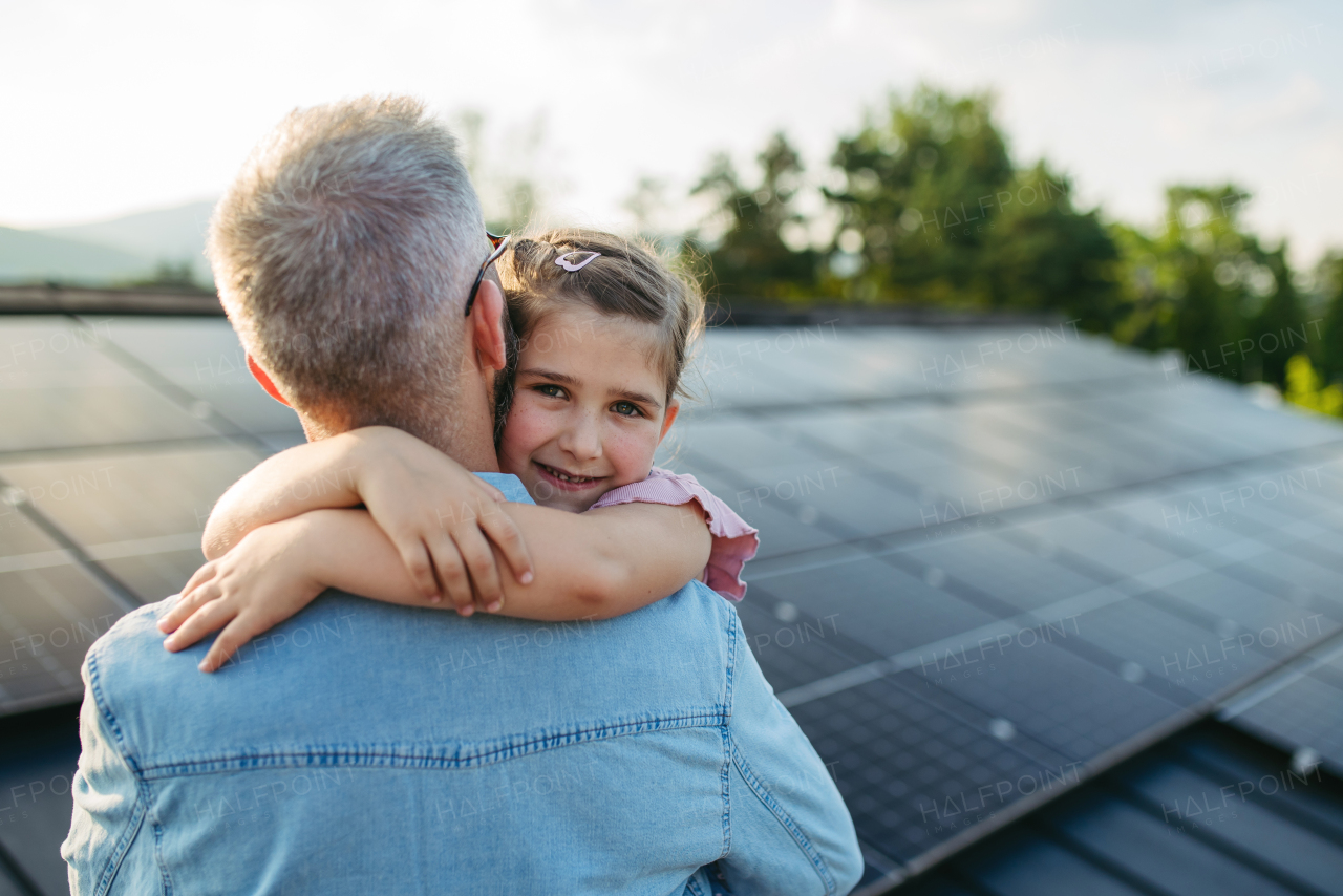 Father with girl on roof with solar panels, hugging. Rooftop solar or photovoltaic system. Sustainable future for next generation concept.