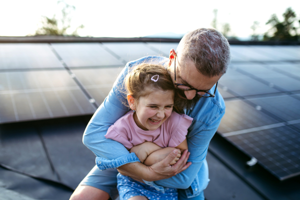 Father with girl on roof with solar panels, hugging. Rooftop solar or photovoltaic system. Sustainable future for next generation concept.