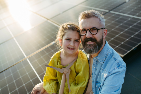 Daughter and father on roof with solar panels, holding model of wind turbine. Rooftop solar or photovoltaic system. Sustainable future for next generation concept.