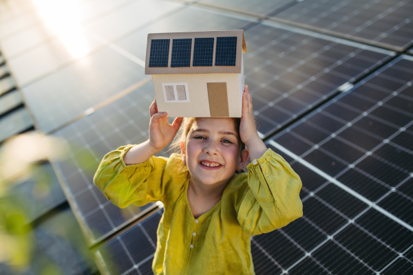 Cute girl holding model of house with solar panels, sitting on rooftop solar or photovoltaic system.