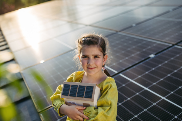 Cute girl holding model of house with solar panels, sitting on rooftop solar or photovoltaic system.