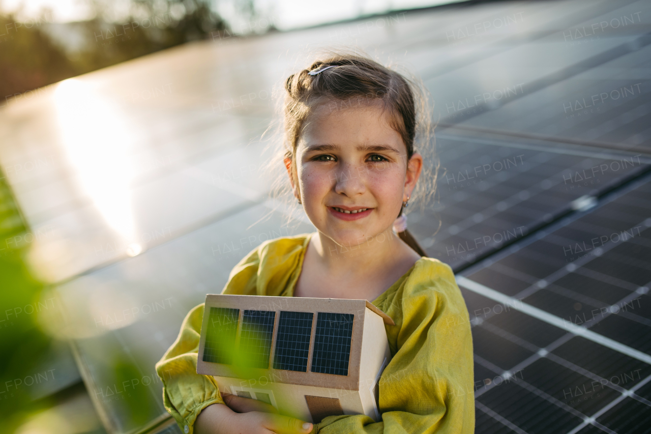 Cute girl holding model of house with solar panels, sitting on rooftop solar or photovoltaic system.