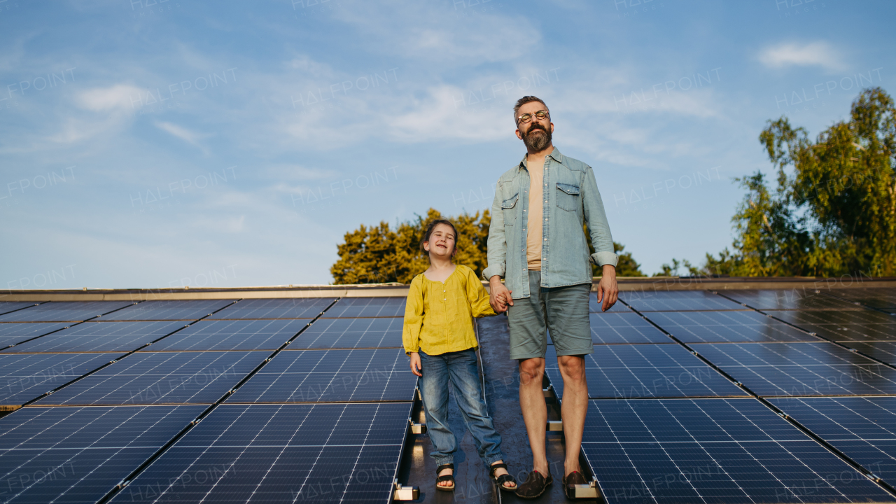 Father standing with girl on roof with solar panels, holding hands. Rooftop solar or photovoltaic system. Sustainable future for next generation concept.