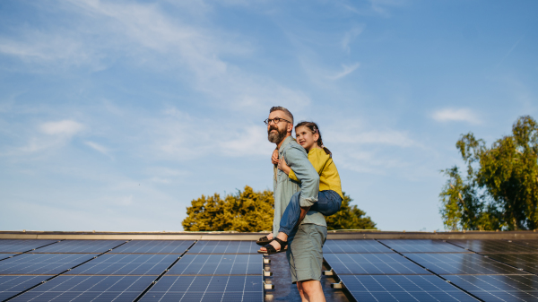 Father with girl on roof with solar panels, piggyback ride. Rooftop solar or photovoltaic system. Sustainable future for next generation concept.