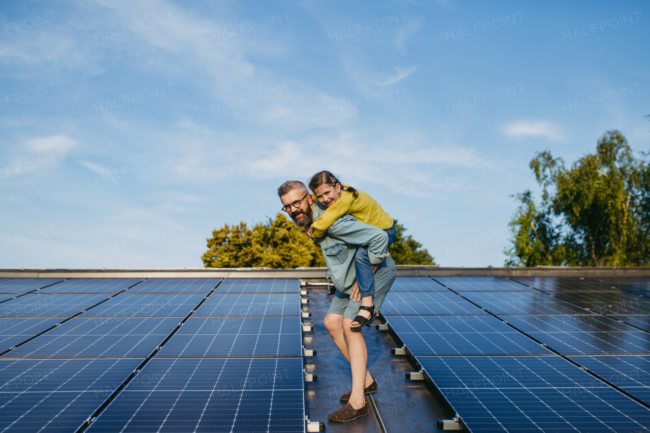 Father with girl on roof with solar panels, piggyback ride. Rooftop solar or photovoltaic system. Sustainable future for next generation concept.