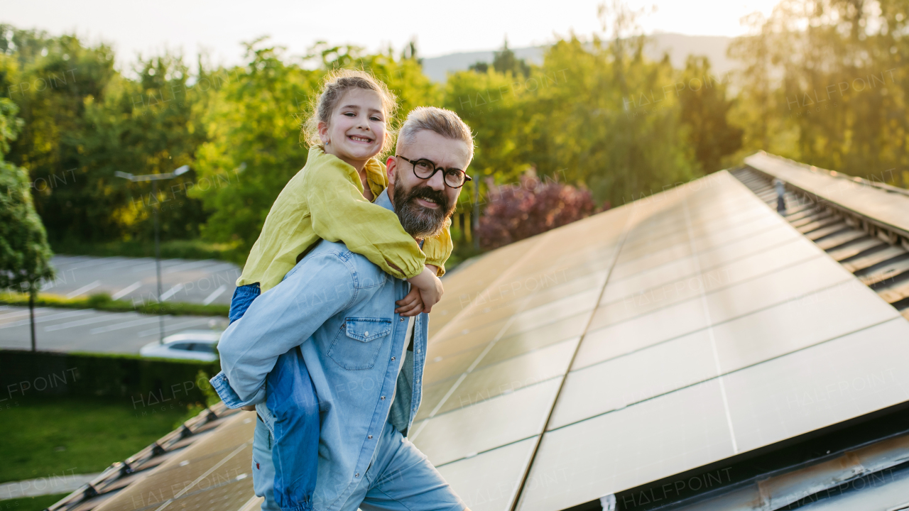 Father with girl on roof with solar panels, piggyback ride. Rooftop solar or photovoltaic system. Sustainable future for next generation concept.