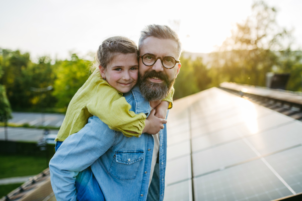 Father with girl on roof with solar panels, piggyback ride. Rooftop solar or photovoltaic system. Sustainable future for next generation concept.