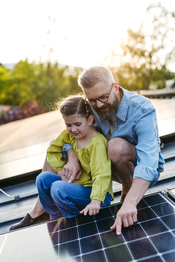 Dad and girl on roof with solar panels, learning about solar energy. Rooftop solar or photovoltaic system. Sustainable future for next generation concept.