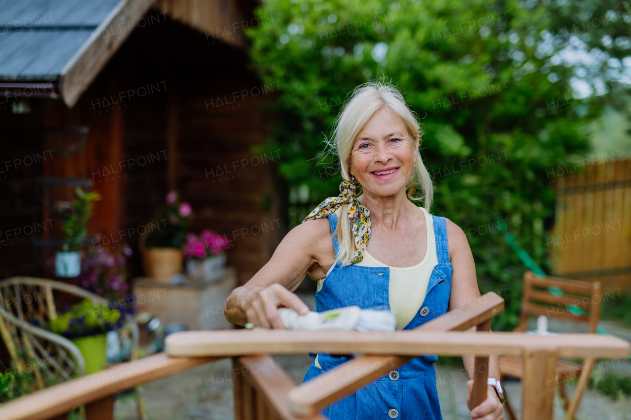 A senior woman cleaning garden furniture and getting the garden ready for summer