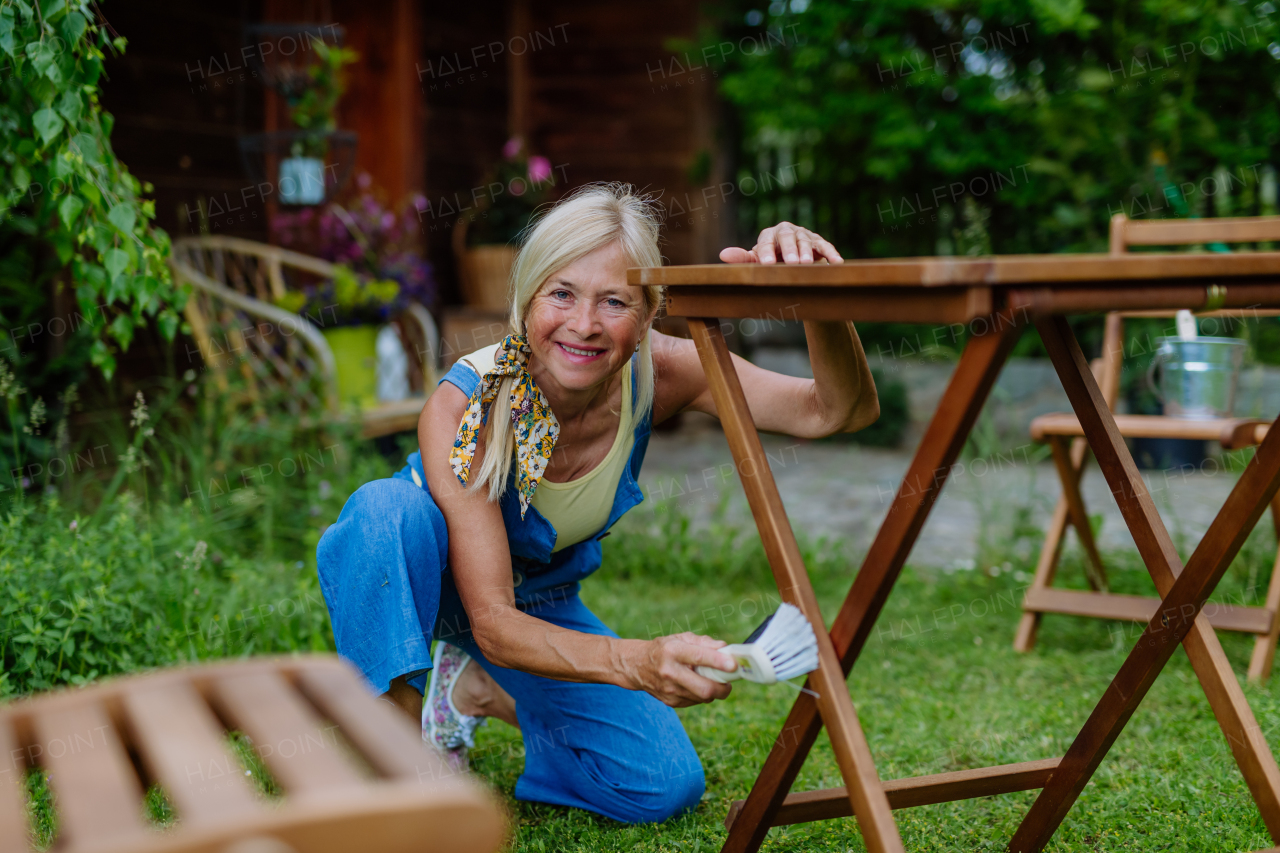 A senior woman cleaning garden furniture and getting the garden ready for summer