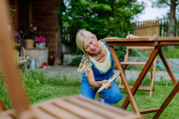 A senior woman cleaning garden furniture and getting the garden ready for summer