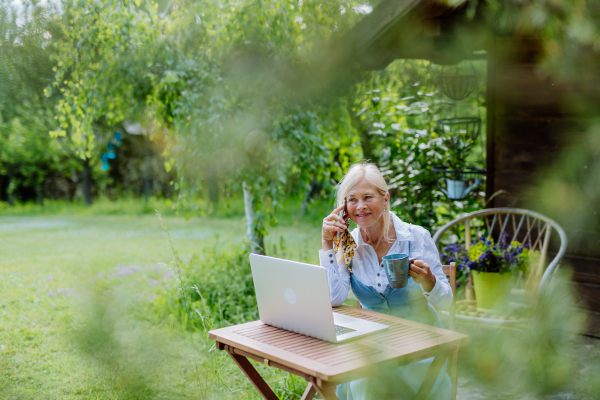 A senior woman with laptop and coffee sitting on terrace in summer, resting.