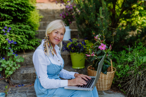 A senior woman with laptop sitting on terrace in summer, resting.