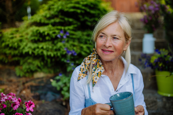 A portrait of senior woman with coffee sitting on terrace in summer, resting and looking at camera.