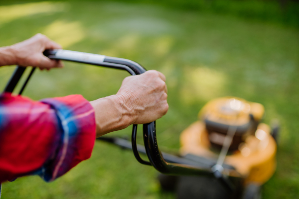 A close-up of elderly woman mowing grass with lawn mower in the garden, garden work concept.