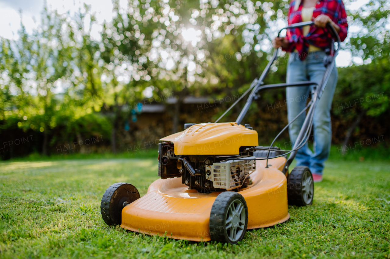 A close-up of woman mowing grass with lawn mower in the garden, garden work concept.