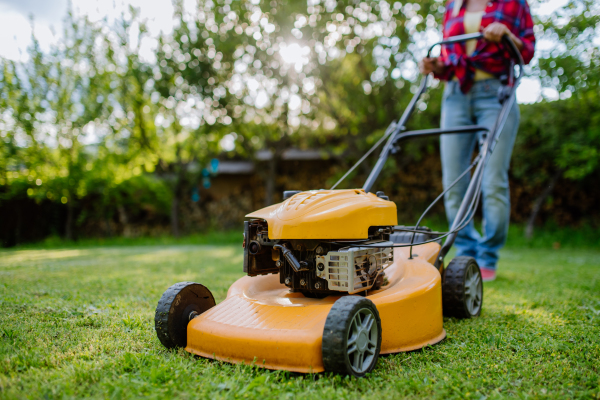 A close-up of woman mowing grass with lawn mower in the garden, garden work concept.