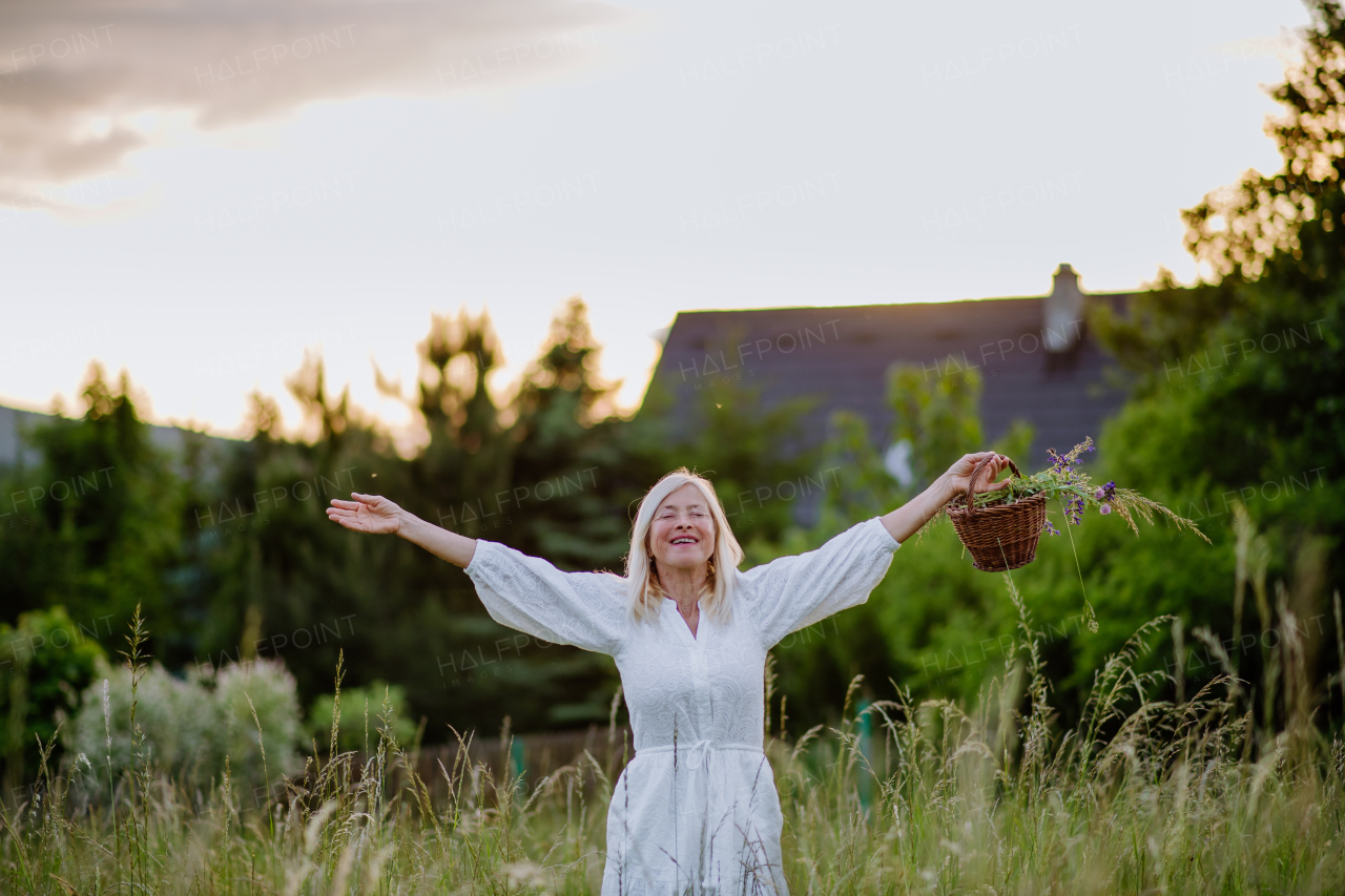 A senior woman with arms outstretched and face up at park on summer day, mental health concept.