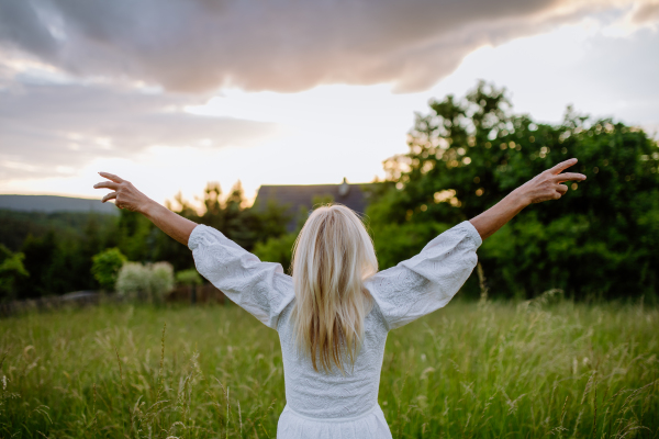 A rear view of senior woman with arms outstretched and face up at park on summer day, mental health concept.