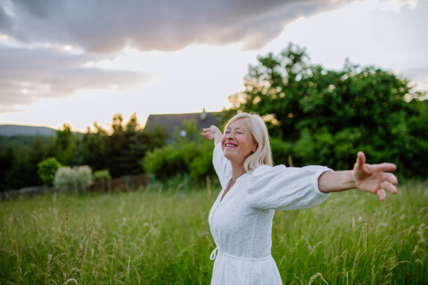 A senior woman with arms outstretched and face up at park on summer day, mental health concept.