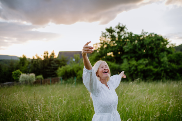 A senior woman with arms outstretched and face up at park on summer day, mental health concept.