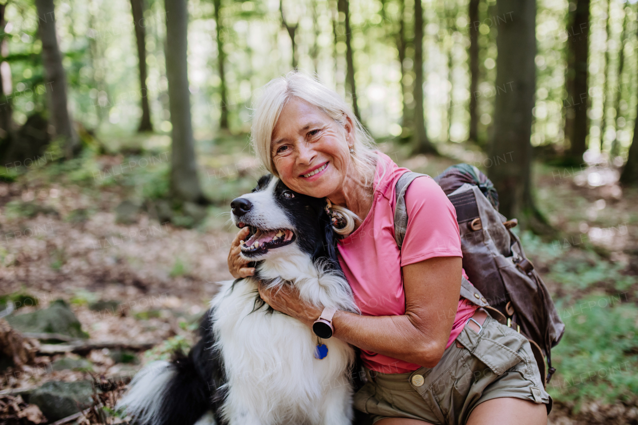 Senior woman resting and stroking her dog during walking in a forest.