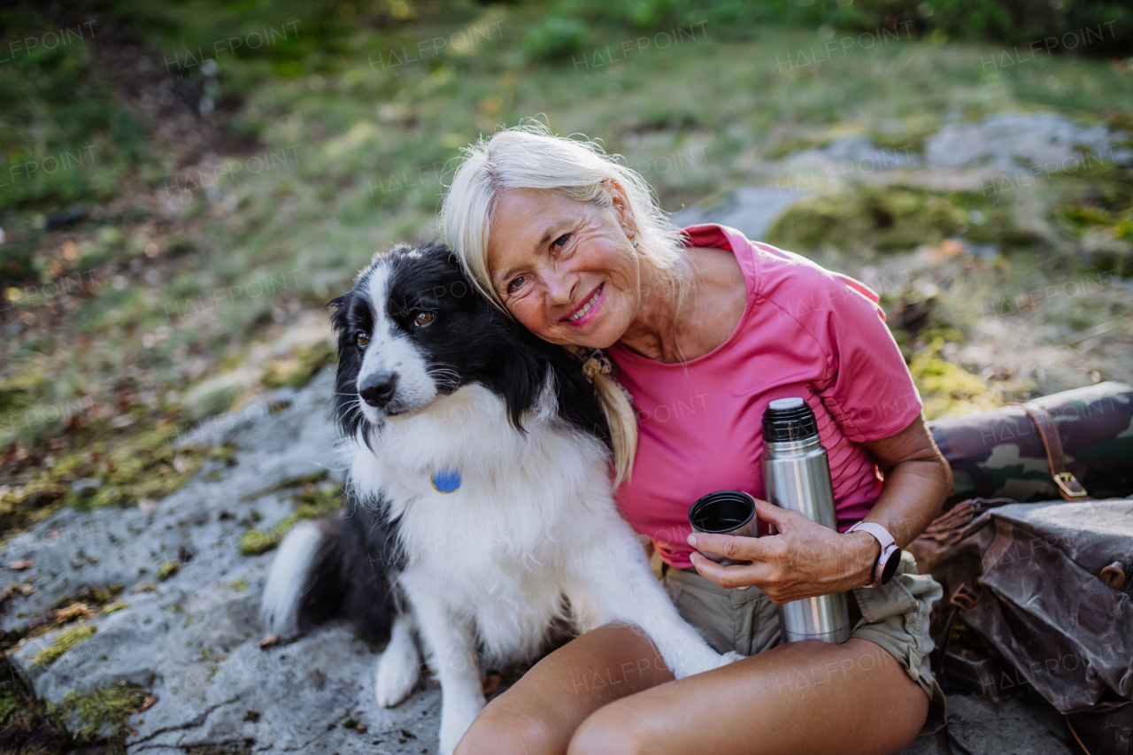 Senior woman having break during walking her dog in a forest.