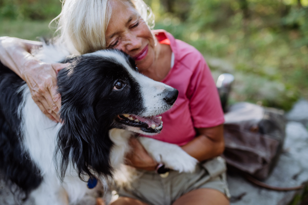 Senior woman resting and stroking her dog during walking in a forest.