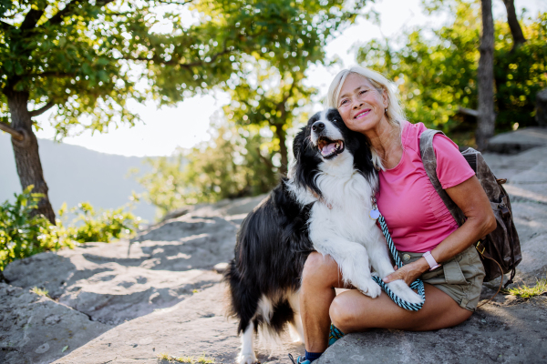 Senior woman resting and stroking her dog during walking in a forest.