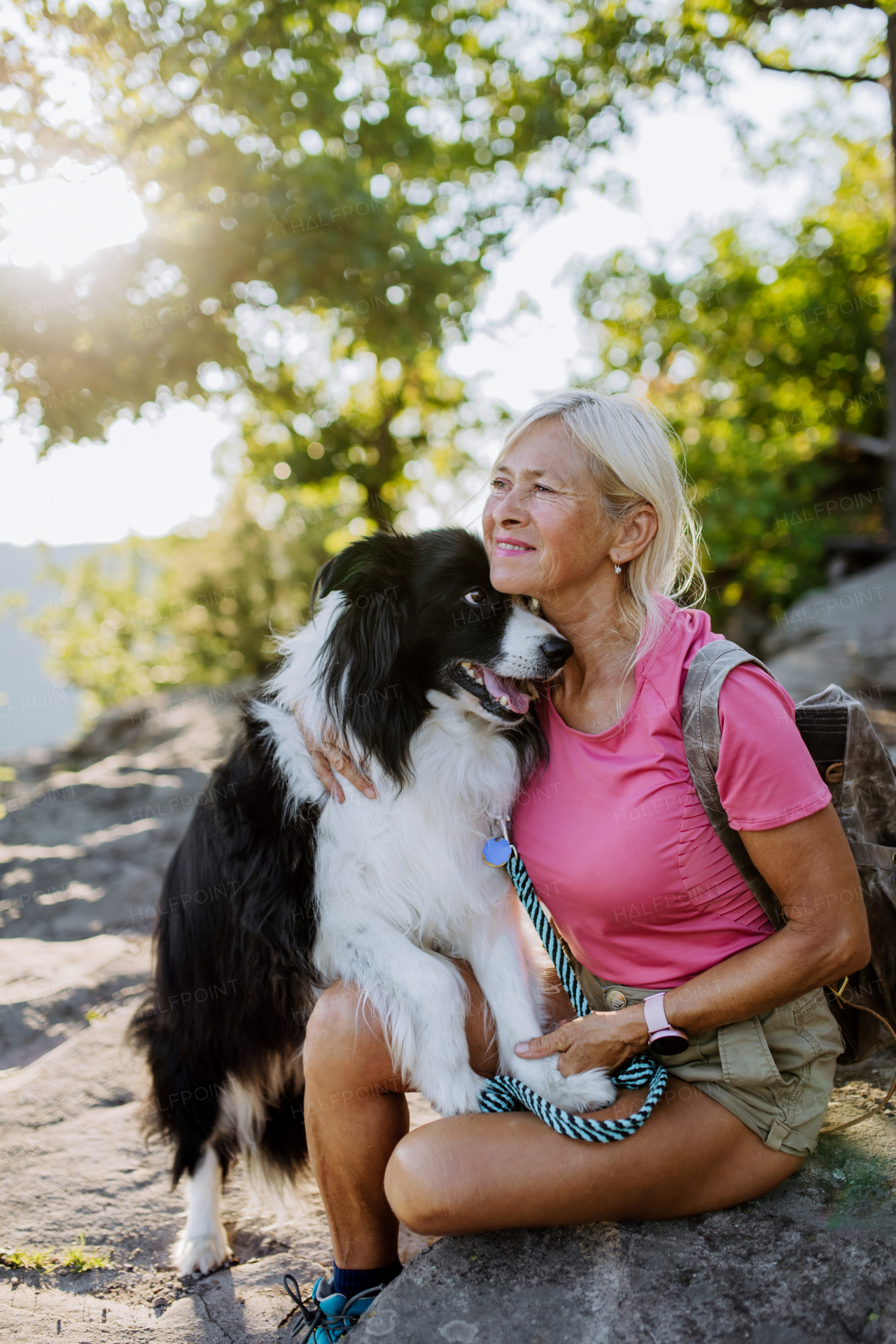 Senior woman resting and stroking her dog during walking in a forest.